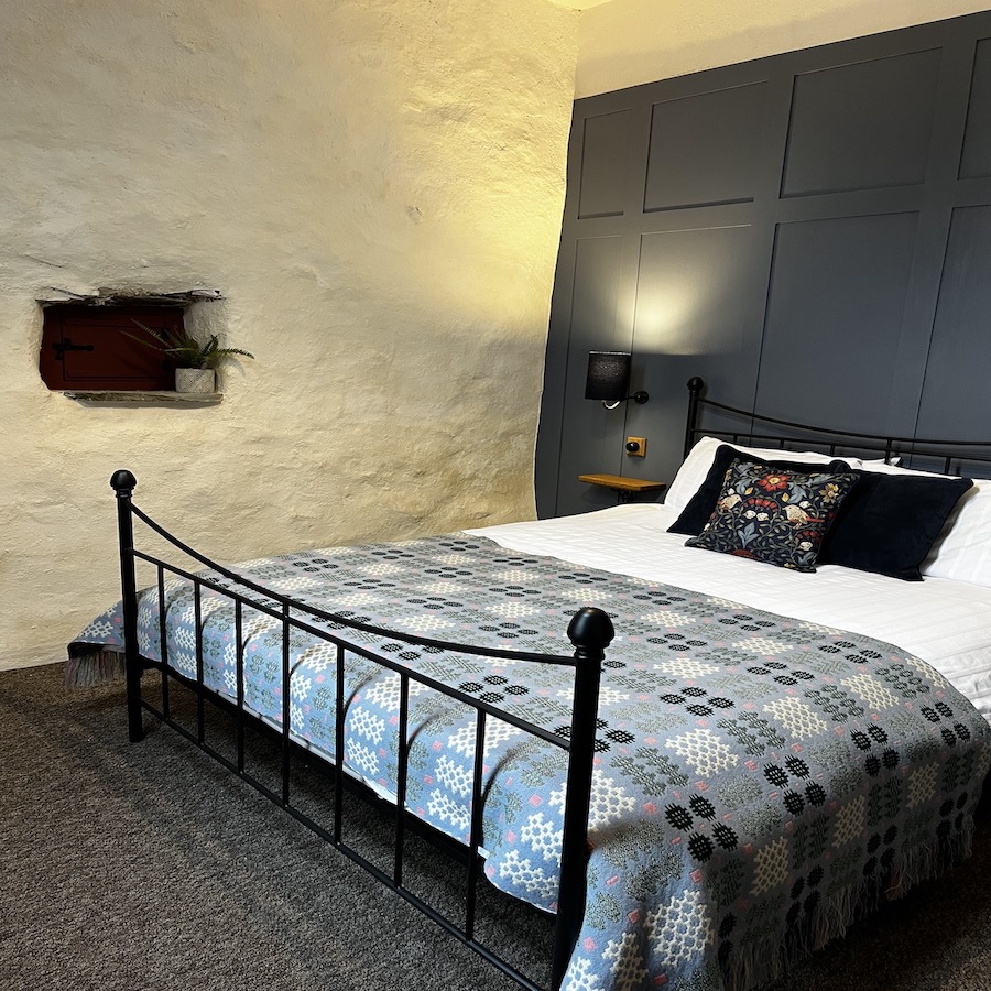 Stablau bedroom, black iron kng size bed, with welsh wool throw. Mid blue wall paneling against lime washed walls.